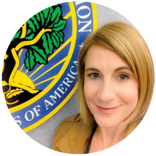 A person with blonde hair takes a selfie next to a colorful emblem featuring a tree against a blue background, capturing the essence of leadership strategies in arts integration.