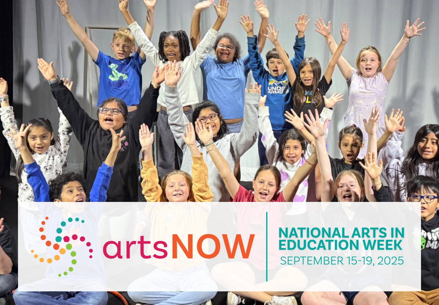 A diverse group of enthusiastic children sit and stand onstage, smiling and raising their hands. The image celebrates arts education with ArtsNOW during National Arts in Education Week, September 15-19, 2025.